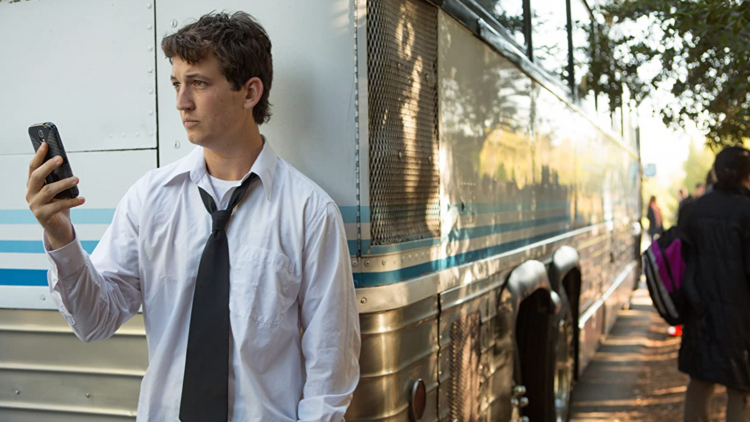 Miles Teller on his phone, leaning on bus