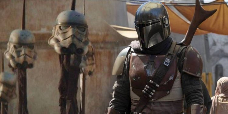 Din Djarin, The Mandalorian, standing by some stormtrooper helmets on spikes.