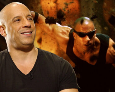 Vin Diesel smiling with a poster of Riddick behind him