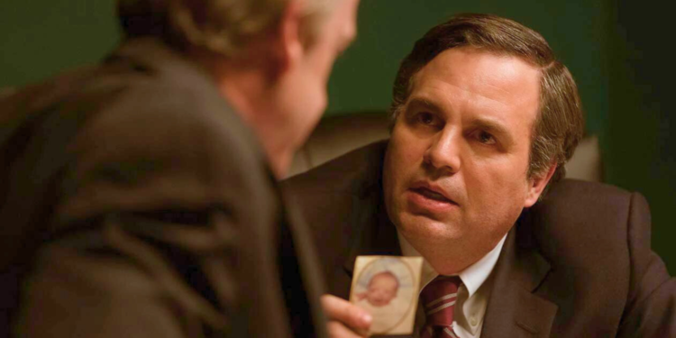 Mark Ruffalo in a suit is holding a card. 