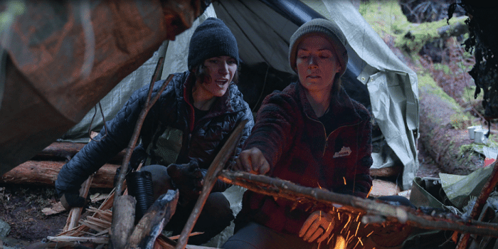 Two female contestants camping around a fire in Outlast